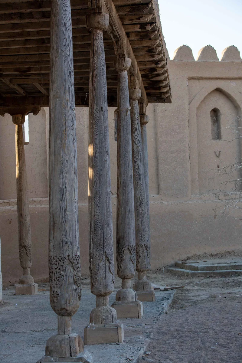 Carved wooden columns supporting a covered walkway beside a clay fortress wall